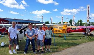 A few of the Aerotrek owners assisting at Aerotrek's AirVentrure 2016 pose in front of a group of airplanes representing many of of the popular model variations offered.